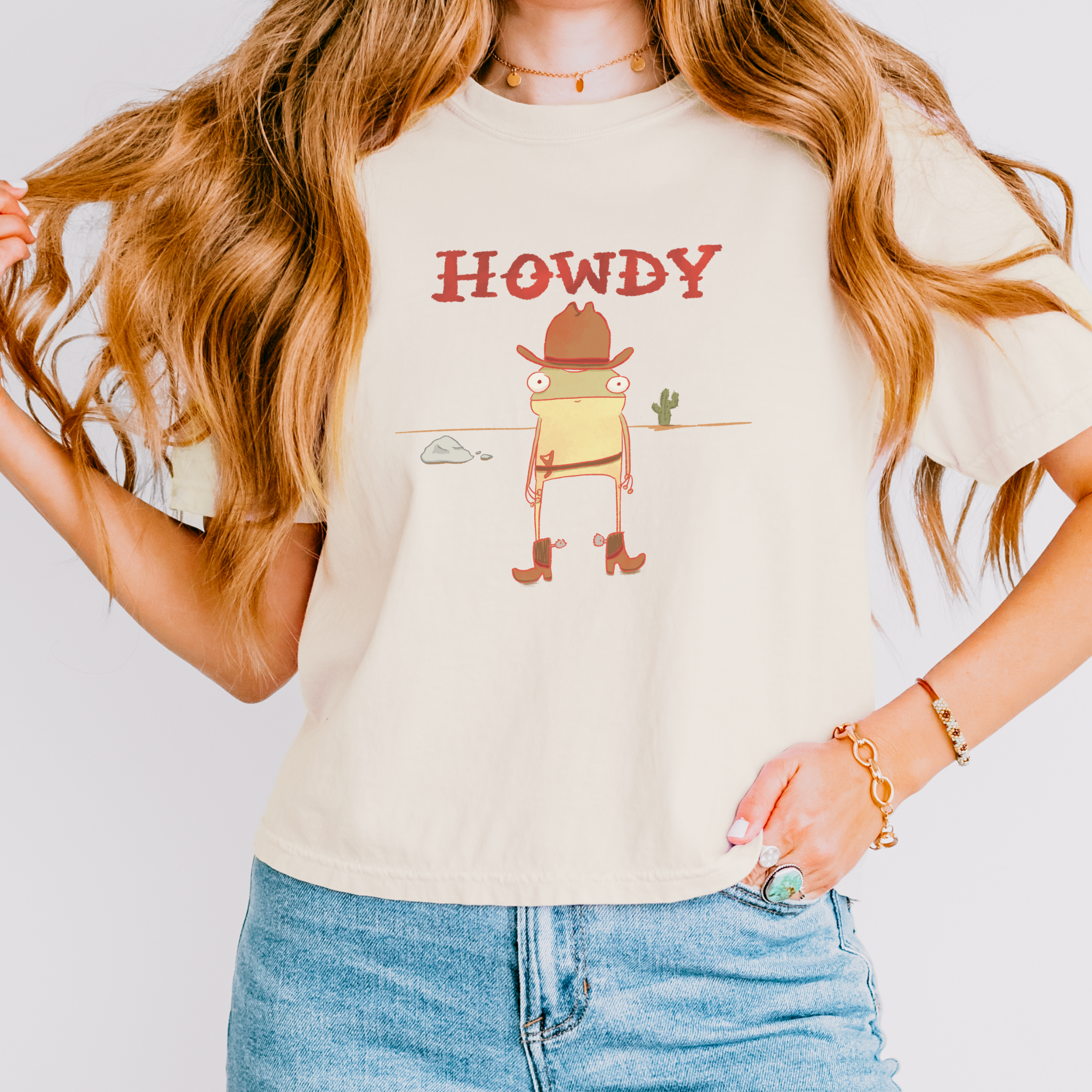 Person wearing a beige t-shirt with a cartoon frog in a cowboy hat and 'HOWDY' text.