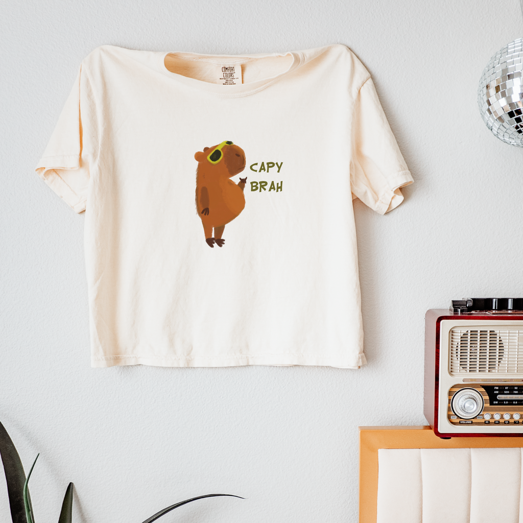 An ivory white boxy fit t-shirt featuring a graphic of a capybara with the text 'CAPY BRAH' on the front.