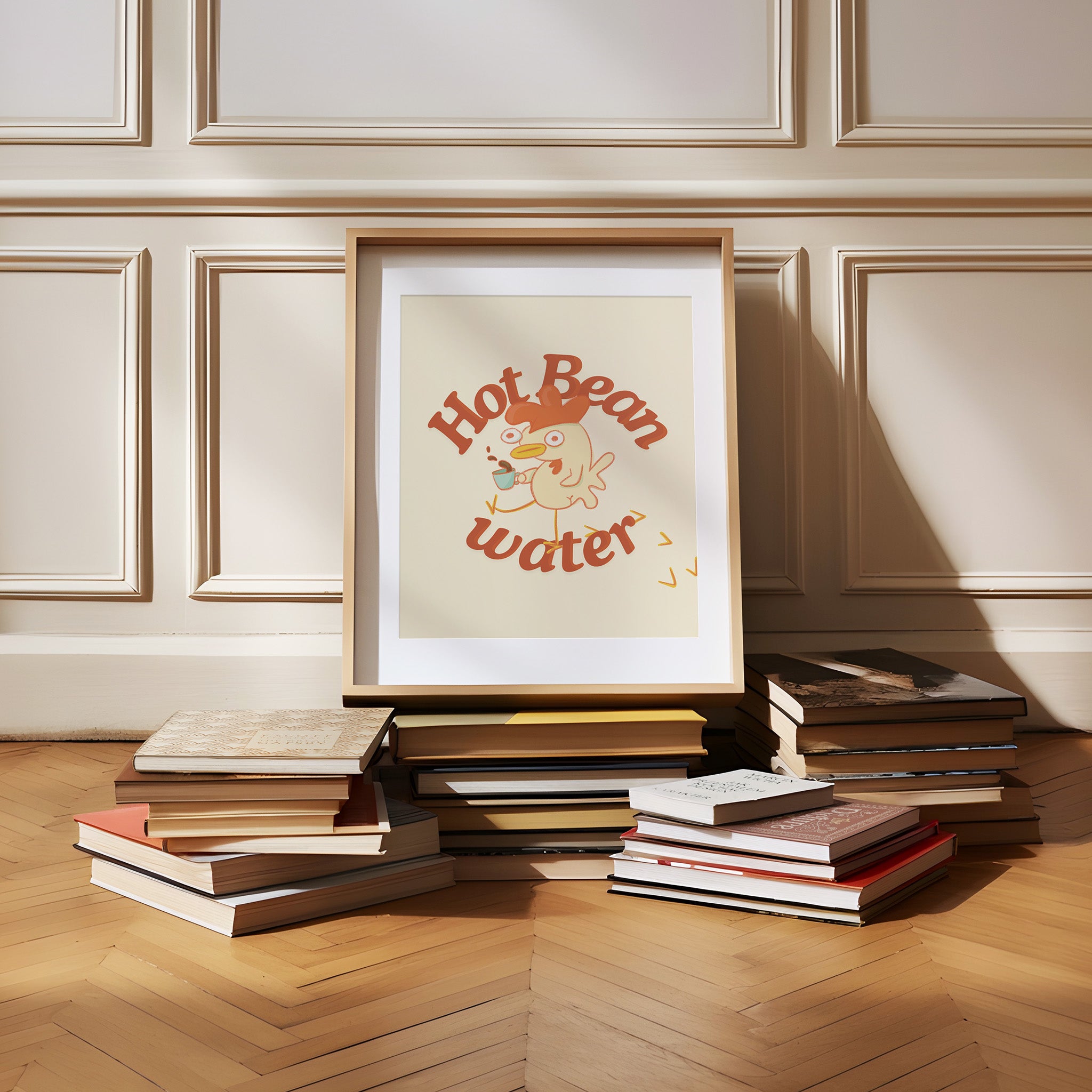 a funny coffee art print that features a chicken holding a cup of coffee next to text that reads "hot bean water" is framed and sitting on a pile of books