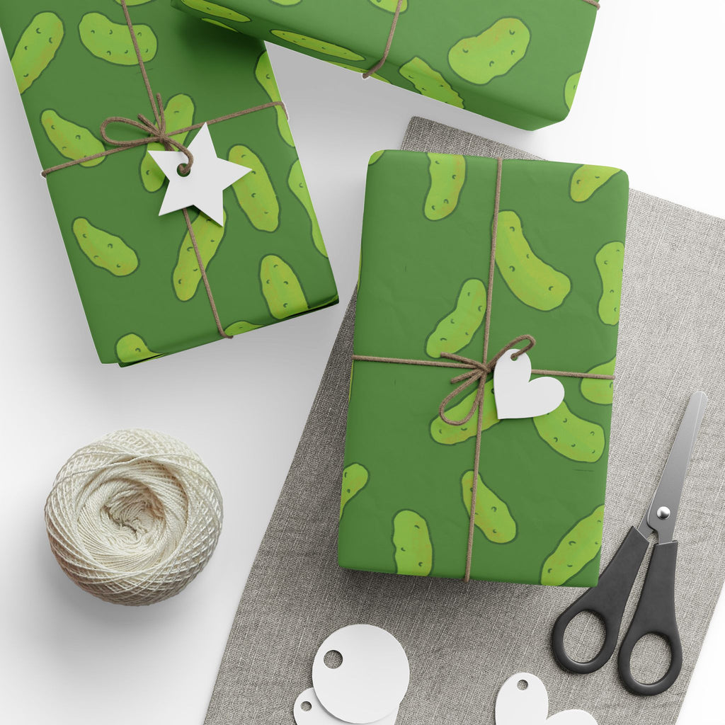 dill pickle wrapping paper that features a pattern of dill pickles over a dark green background is shown wrapped onto several gifts and presents next to twine and scissors