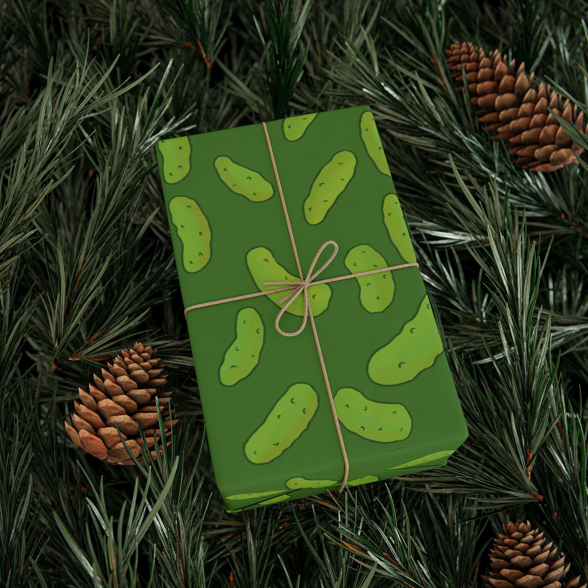 dill pickle wrapping paper that features a pattern of dill pickles over a dark green background is used to wrap a boxed gift with twine and rested on a Christmas tree
