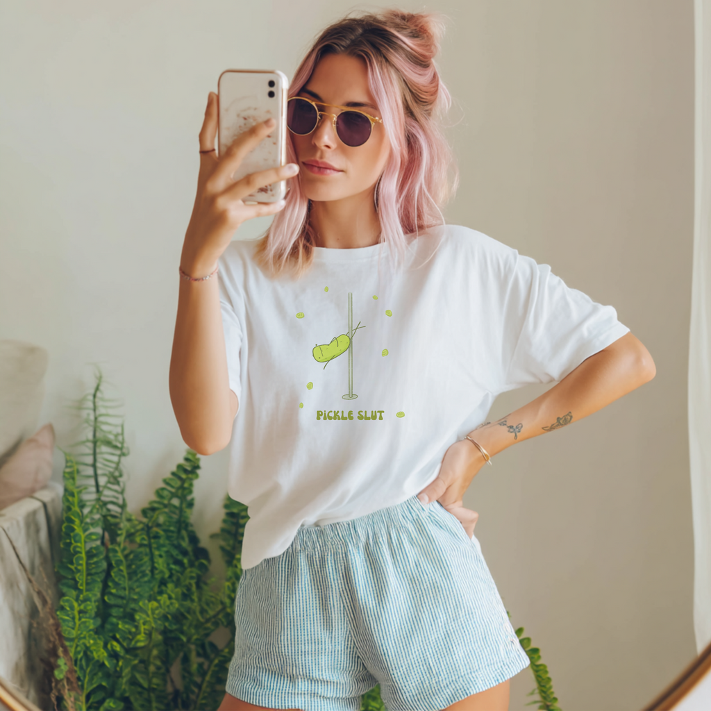 woman with pink hair wearing a pickle slut t-shirt standing next to a house plant