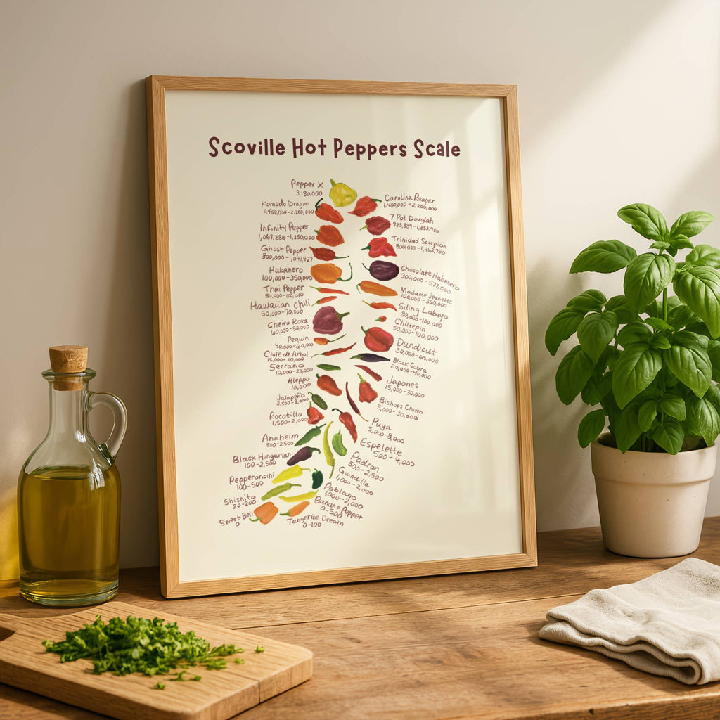 chili pepper print is displayed in a wooden frame on a kitchen counter next to a basil plant and olive oil jar